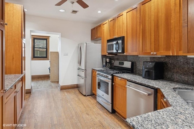 kitchen with visible vents, light wood-style floors, appliances with stainless steel finishes, light stone countertops, and tasteful backsplash