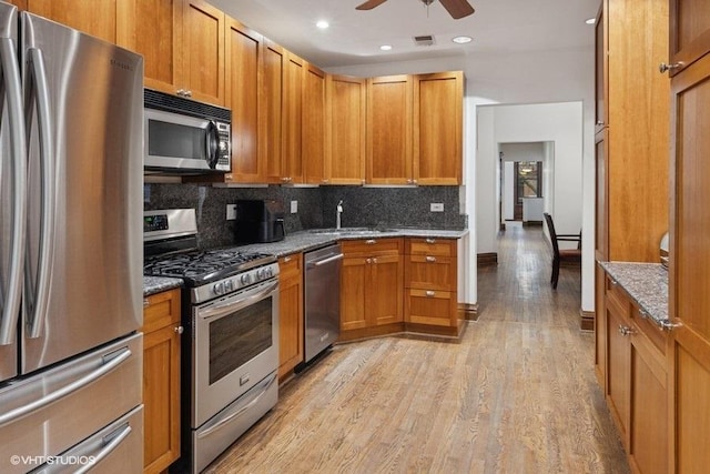 kitchen with stone countertops, a sink, appliances with stainless steel finishes, light wood-type flooring, and decorative backsplash