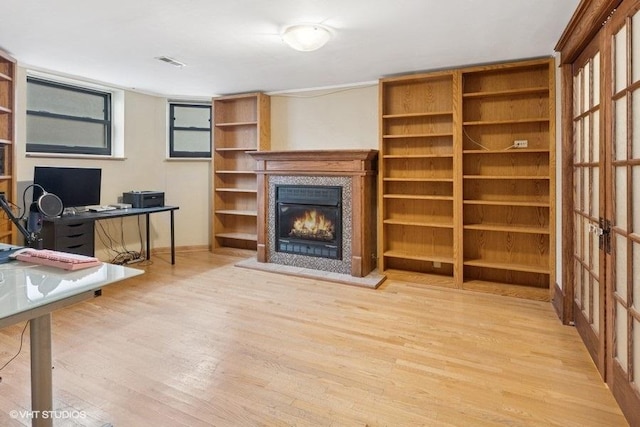 unfurnished office featuring a glass covered fireplace, visible vents, and wood finished floors