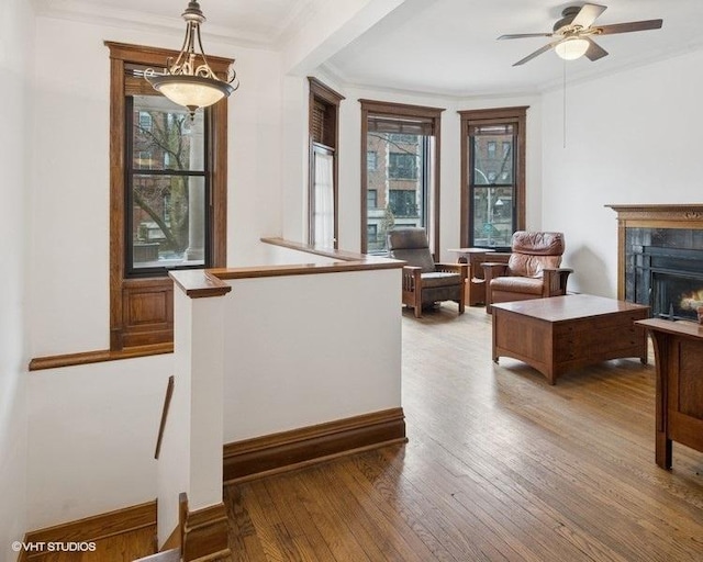 interior space with ceiling fan, a high end fireplace, baseboards, light wood finished floors, and crown molding