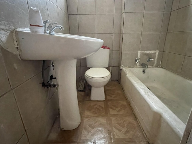 full bathroom featuring a washtub, tile walls, and toilet