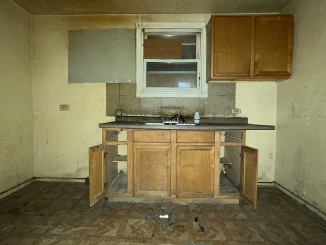 kitchen featuring tasteful backsplash, dark countertops, brown cabinets, and a sink