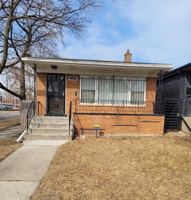 view of front of house with a porch, brick siding, and a chimney