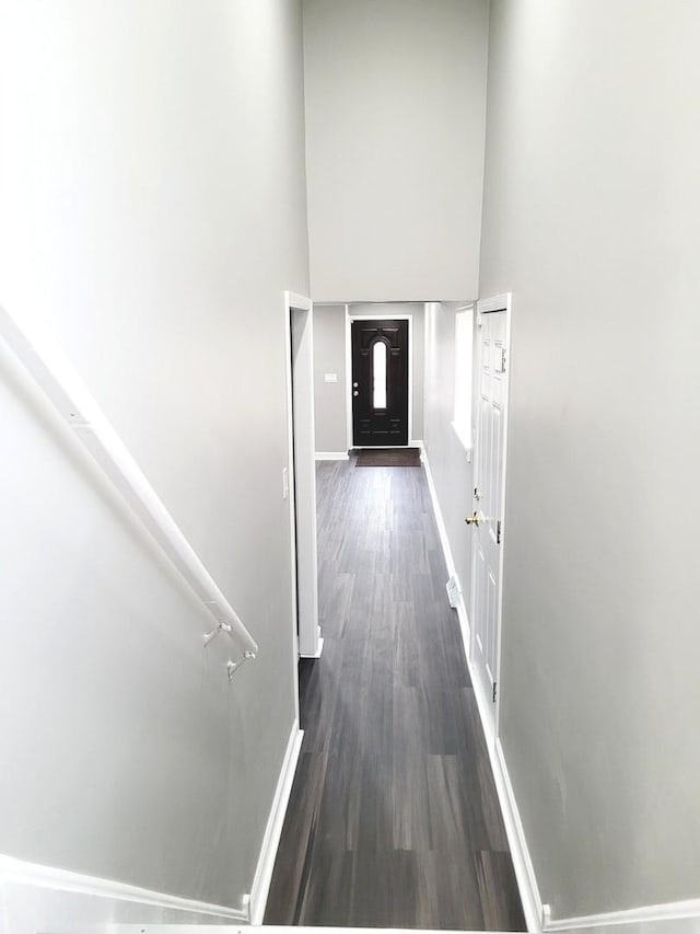 hall featuring a high ceiling, baseboards, and dark wood finished floors