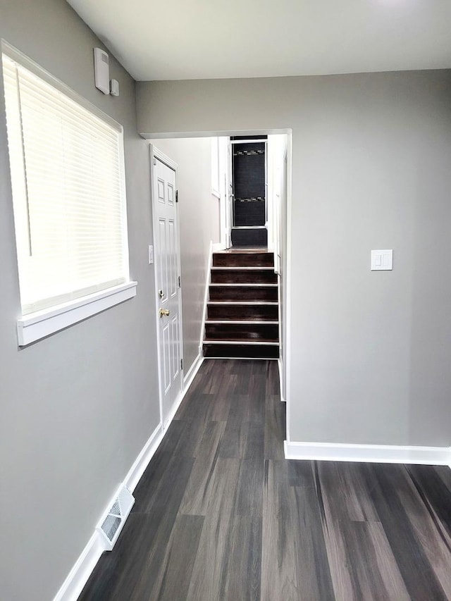 corridor with dark wood-style floors, stairway, and baseboards