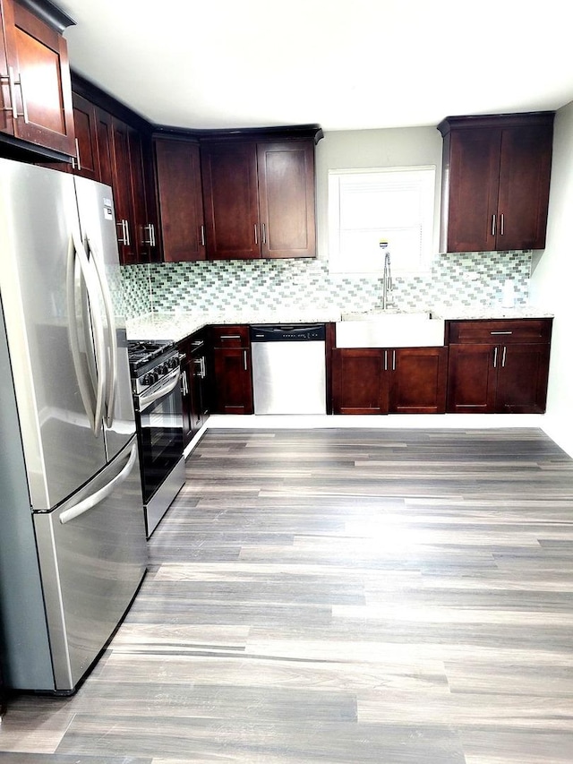 kitchen featuring stainless steel appliances, a sink, light wood-style floors, light countertops, and decorative backsplash