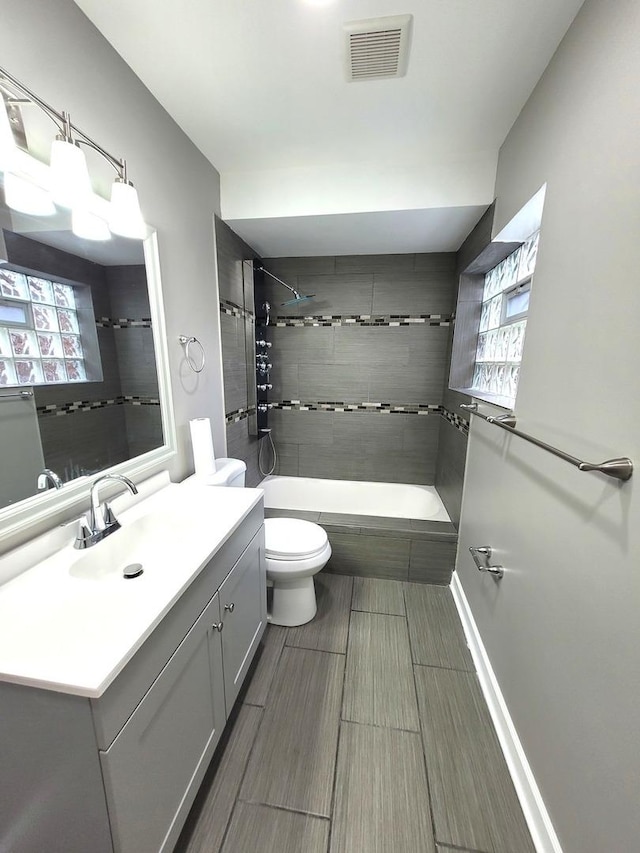 bathroom with tiled shower / bath, visible vents, toilet, vanity, and baseboards