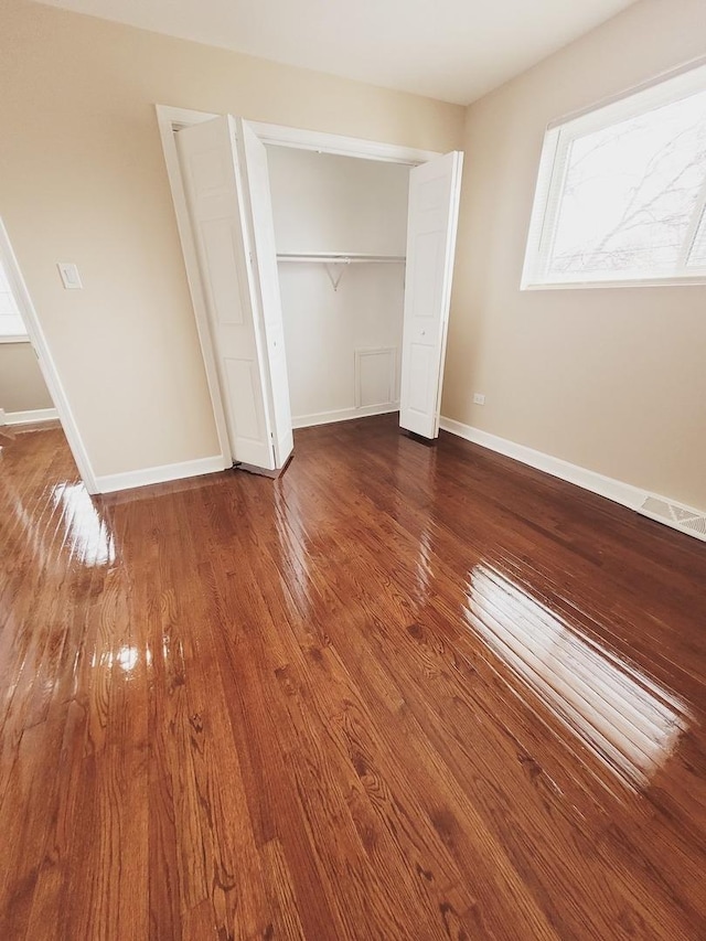 unfurnished bedroom with a closet, hardwood / wood-style floors, and baseboards