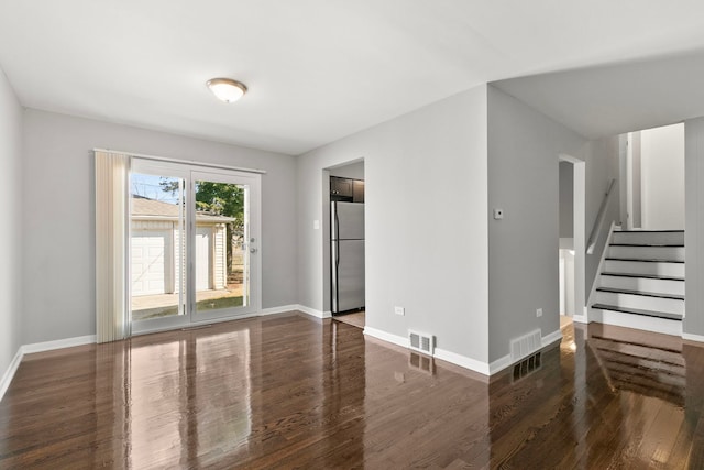 unfurnished living room with visible vents, baseboards, wood finished floors, and stairway