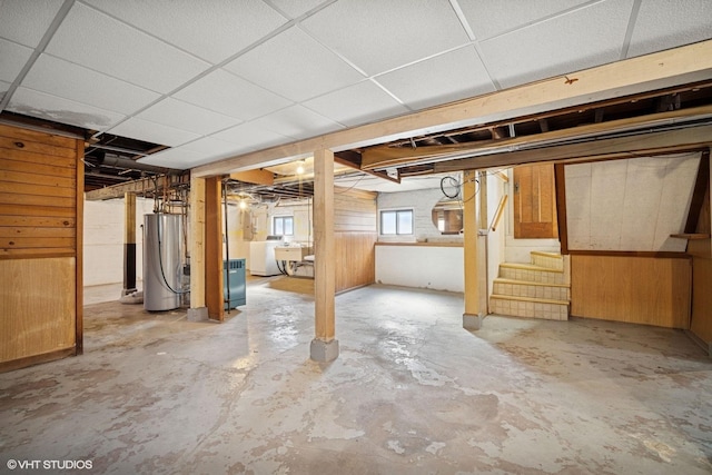 below grade area with a paneled ceiling, wooden walls, water heater, stairs, and washer / clothes dryer