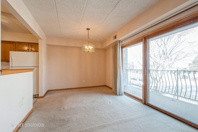 unfurnished dining area featuring light carpet, a textured ceiling, baseboards, and a notable chandelier