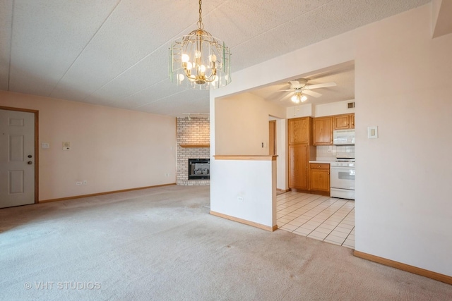 unfurnished living room featuring a brick fireplace, ceiling fan with notable chandelier, baseboards, and light colored carpet