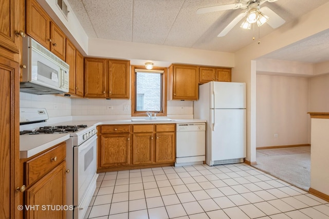 kitchen featuring white appliances, a sink, light countertops, decorative backsplash, and brown cabinetry