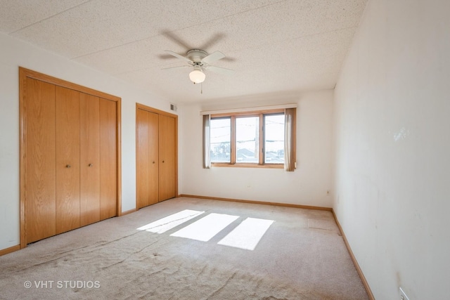 unfurnished bedroom with multiple closets, carpet, visible vents, and baseboards