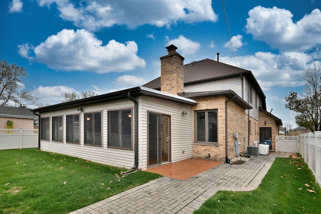 back of house with a lawn, a patio, a fenced backyard, a chimney, and brick siding