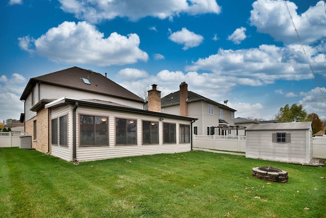 back of property with an outbuilding, a fenced backyard, a lawn, and a fire pit