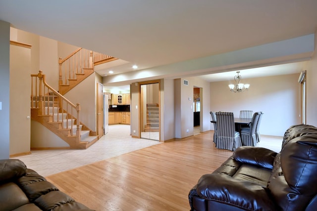 living room with visible vents, a notable chandelier, light wood-style flooring, and stairs