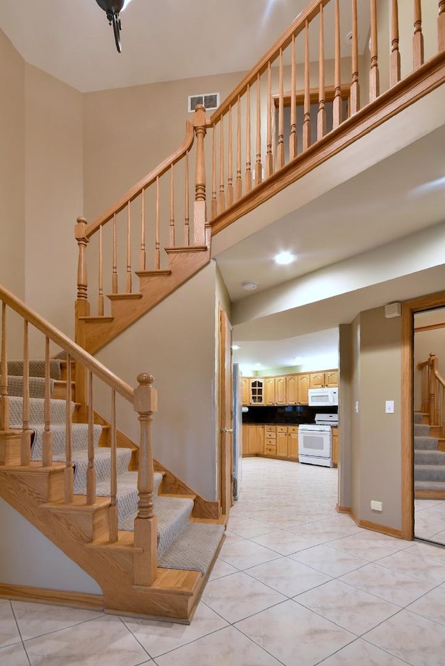 stairs featuring baseboards, a high ceiling, visible vents, and tile patterned floors