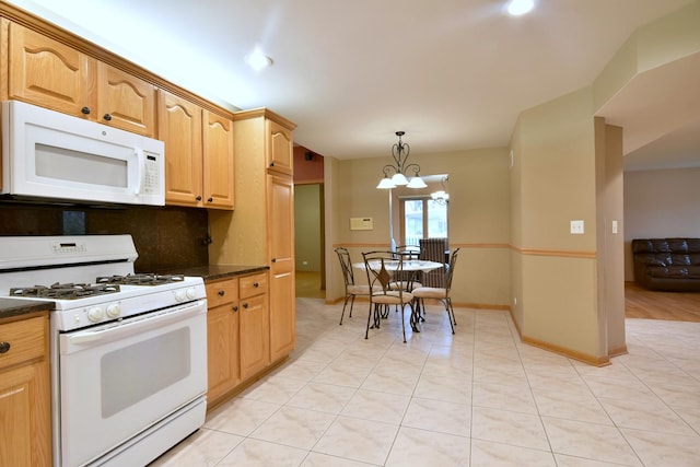 kitchen featuring white appliances, light tile patterned floors, dark countertops, an inviting chandelier, and pendant lighting