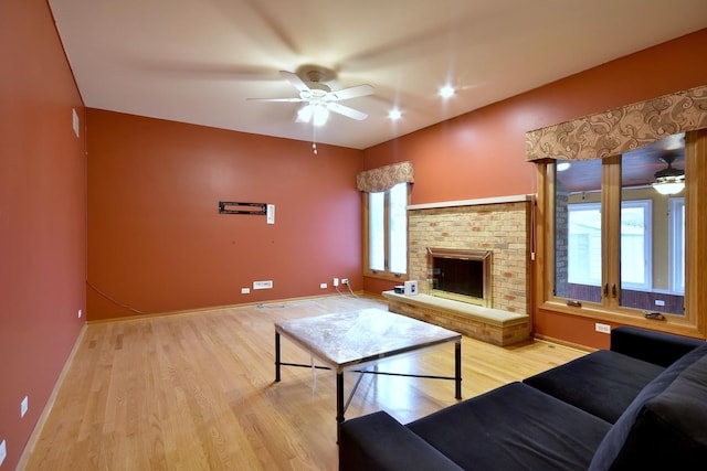 living area with a brick fireplace, ceiling fan, baseboards, and wood finished floors