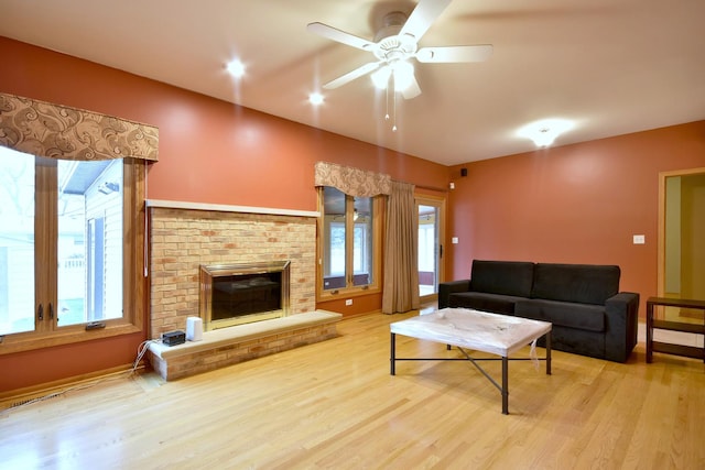 living room featuring a brick fireplace, ceiling fan, and light wood finished floors