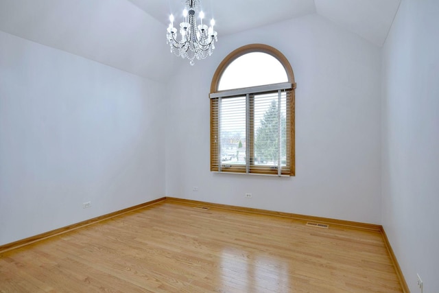 unfurnished room with lofted ceiling, visible vents, an inviting chandelier, wood finished floors, and baseboards