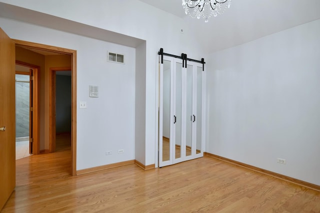 spare room featuring baseboards, visible vents, light wood finished floors, and a barn door