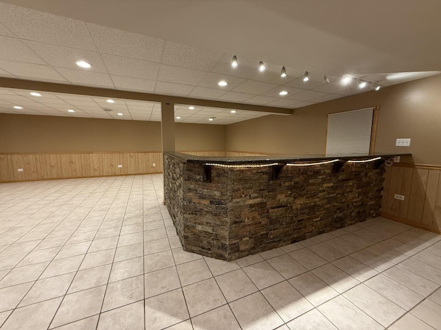 bar with a bar, a wainscoted wall, light tile patterned flooring, and wood walls