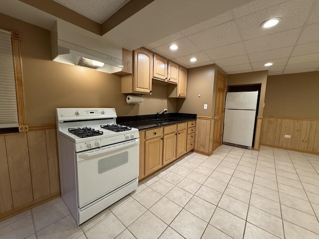 kitchen featuring a sink, white appliances, dark countertops, and a wainscoted wall