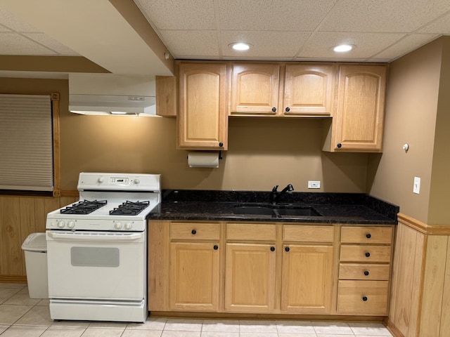 kitchen with a wainscoted wall, white gas stove, a sink, dark stone countertops, and under cabinet range hood