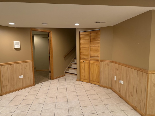 finished basement featuring visible vents, a wainscoted wall, stairway, wood walls, and light tile patterned flooring