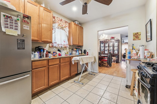 kitchen with black gas range, light tile patterned floors, brown cabinetry, a ceiling fan, and freestanding refrigerator