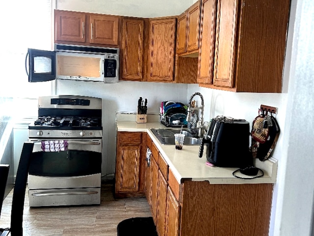 kitchen featuring light wood-style flooring, appliances with stainless steel finishes, brown cabinets, light countertops, and a sink