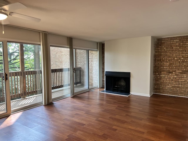 unfurnished living room featuring a fireplace with raised hearth, brick wall, ceiling fan, and wood finished floors