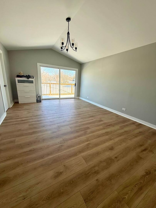 unfurnished dining area featuring a chandelier, vaulted ceiling, wood finished floors, and baseboards