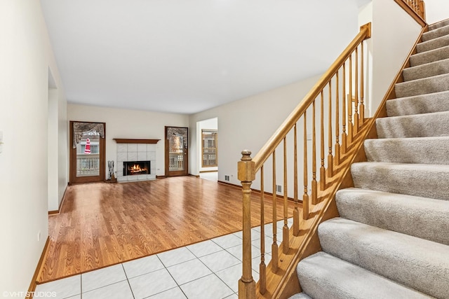 unfurnished living room featuring stairs, light tile patterned flooring, a fireplace, and baseboards