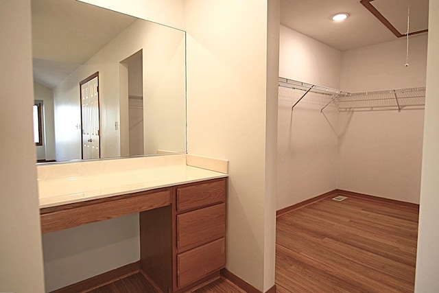 walk in closet with attic access, dark wood-type flooring, and built in study area