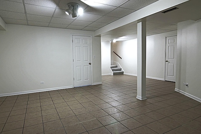 finished basement featuring a paneled ceiling, visible vents, stairway, and baseboards