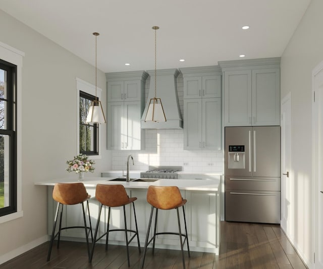 kitchen featuring tasteful backsplash, stainless steel fridge with ice dispenser, light countertops, premium range hood, and a kitchen bar