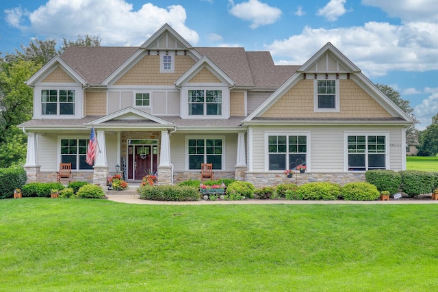 craftsman house featuring a porch, a front yard, stone siding, and a shingled roof