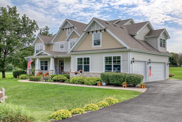 view of front of house with roof with shingles, a garage, stone siding, driveway, and a front lawn