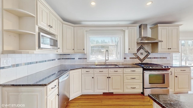 kitchen with tasteful backsplash, dark stone countertops, stainless steel appliances, wall chimney range hood, and a sink