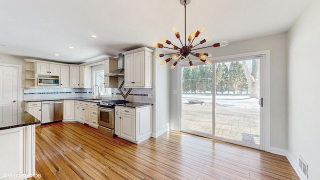 kitchen featuring a sink, appliances with stainless steel finishes, wall chimney exhaust hood, backsplash, and open shelves