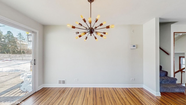 unfurnished dining area with baseboards, visible vents, stairway, wood finished floors, and a notable chandelier