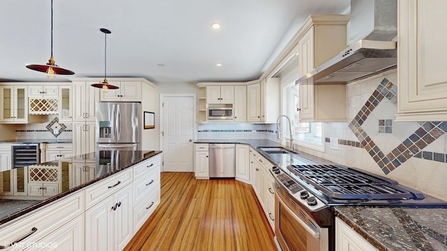 kitchen with light wood finished floors, beverage cooler, stainless steel appliances, wall chimney range hood, and a sink