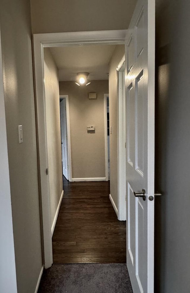 hallway featuring carpet, wood finished floors, and baseboards