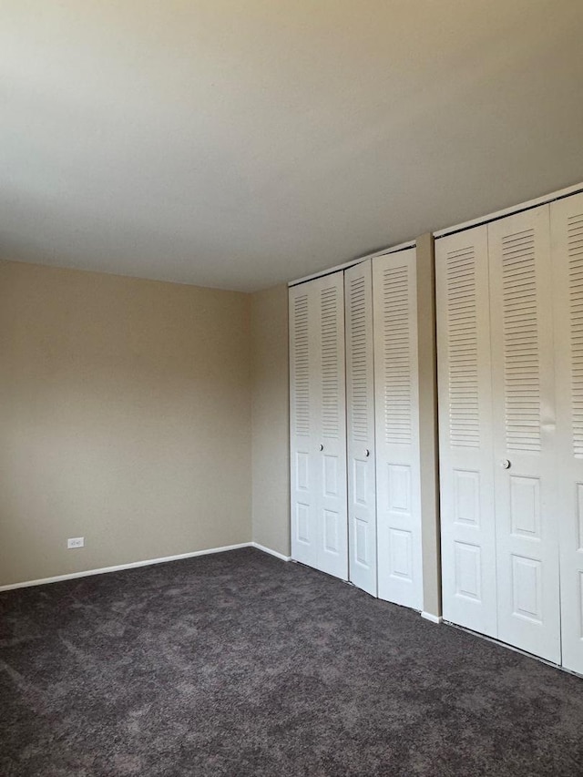 unfurnished bedroom with two closets, baseboards, and carpet flooring