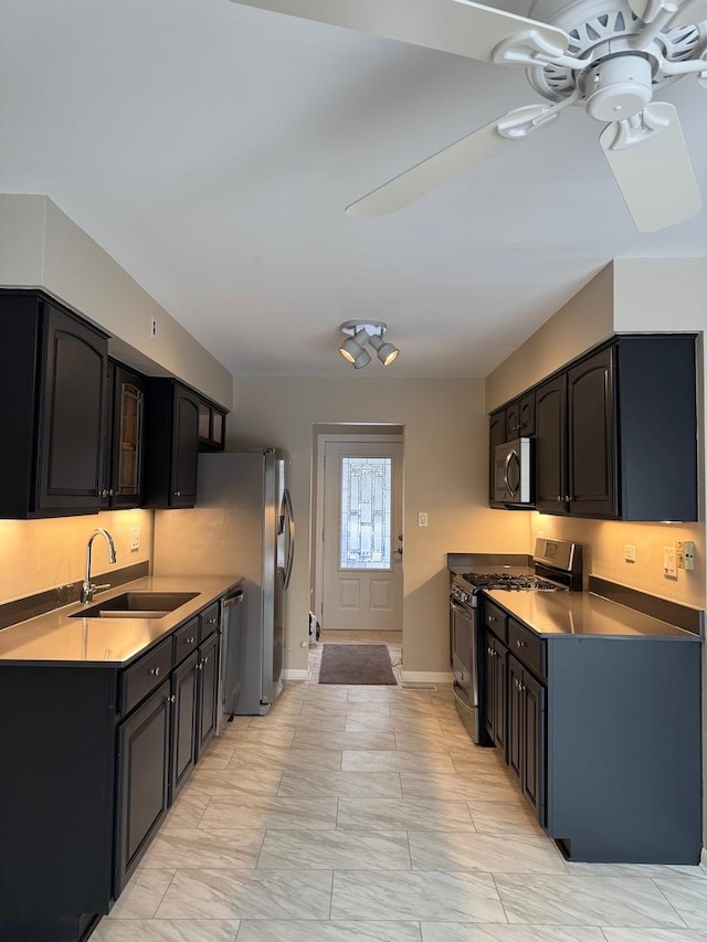 kitchen with appliances with stainless steel finishes, a sink, a ceiling fan, and baseboards