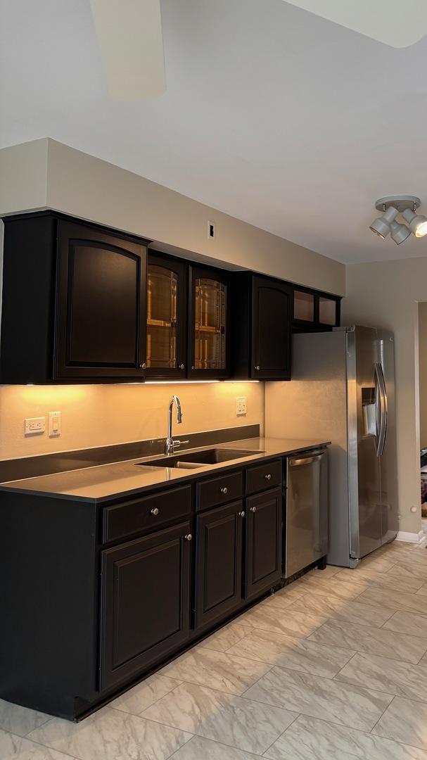 kitchen featuring glass insert cabinets, appliances with stainless steel finishes, marble finish floor, dark cabinetry, and a sink