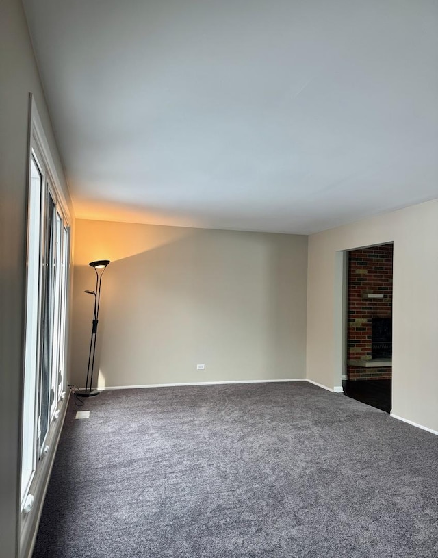 spare room with a brick fireplace, baseboards, and dark colored carpet